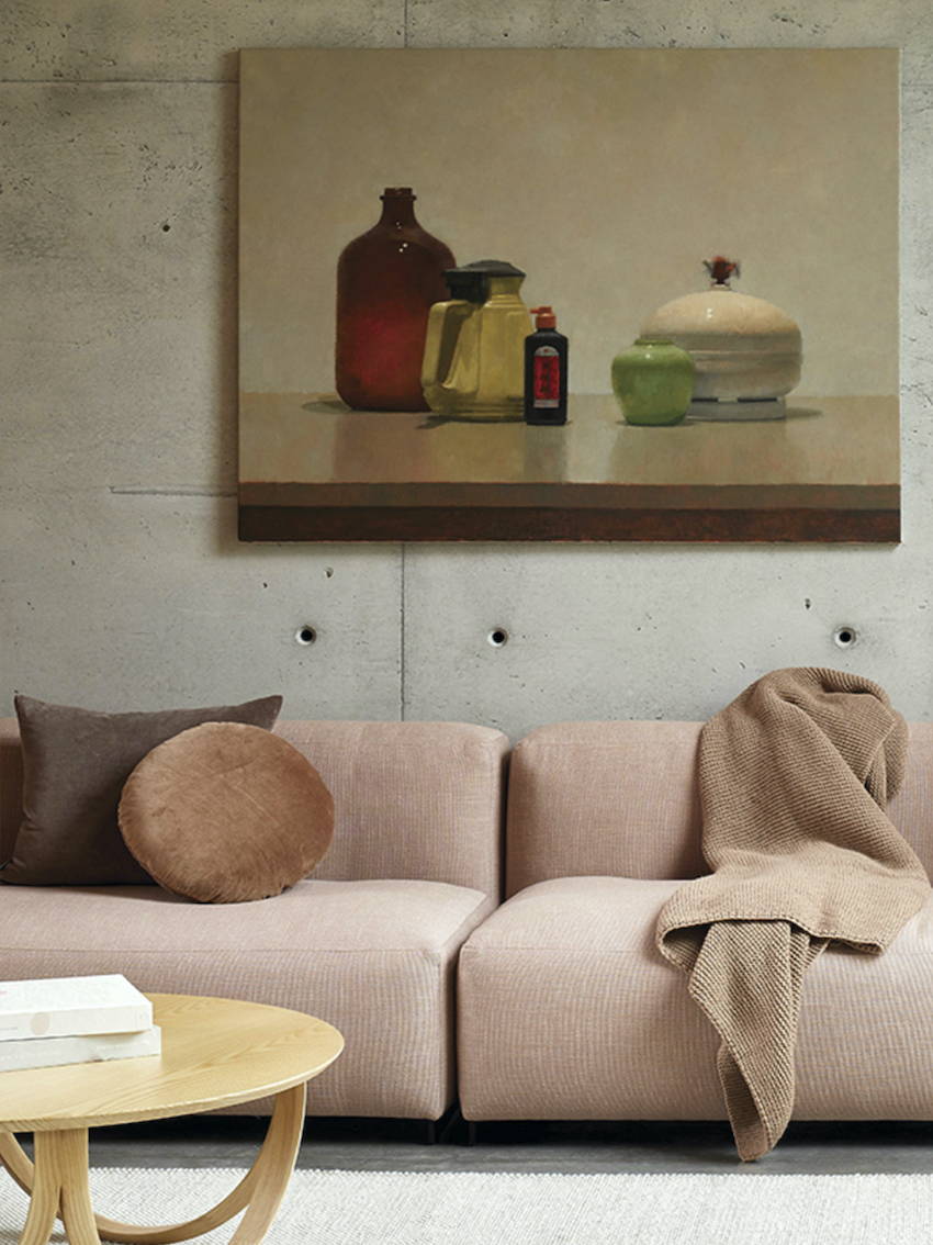 A lounge room setting with a pink sofa dressed with beautiful cushions and throws and a still life artwork on the wall.