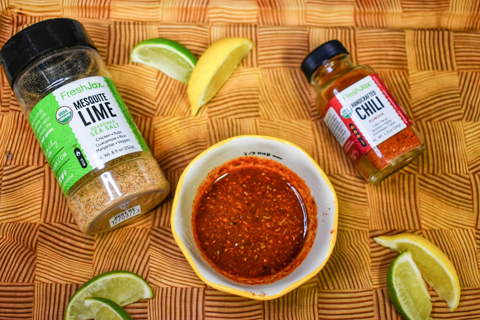 FreshJax Organic Mesquite Lime seasoned sea salt and Handcrafted Chili seasoning on cutting board with lime wedges and chili sauce