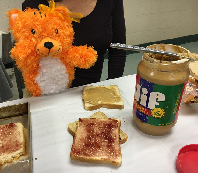Primrose puppet Katie the cat sits by a table with open peanut butter and jelly bread slices