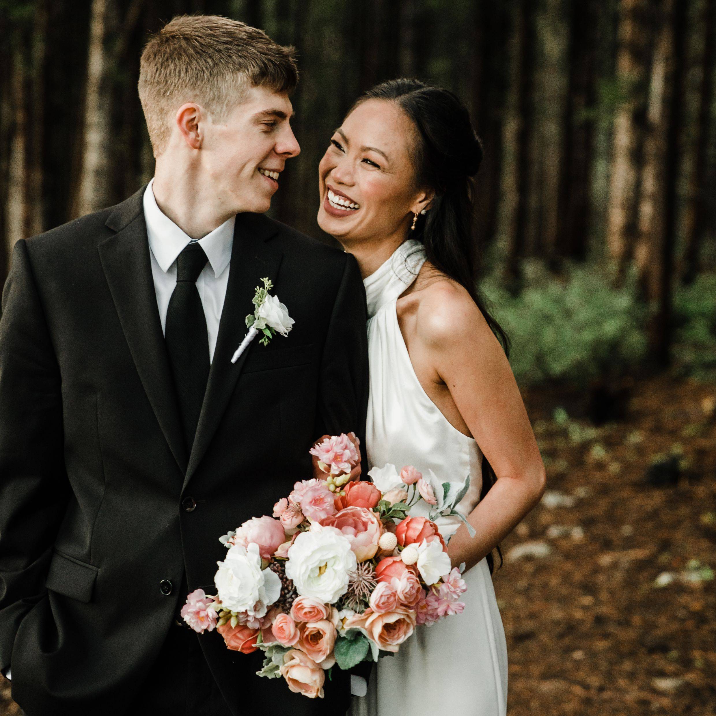 Coral, peach, and white unstructured bridal bouquet being held by a bride and groom in the mountains of Colorado