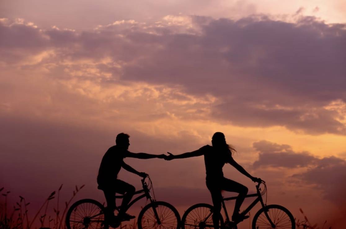 Woman on bike reaching back for man’s hand also on bike