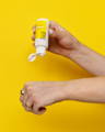 Model pores Clear Skin Days Clarifying Serum onto the back of their left hand. This has a yellow background