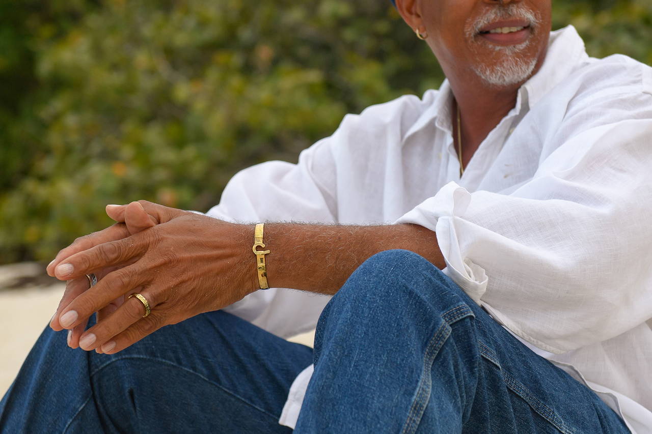 Man sitting on the beach wearing a Vibe Jewelry 14K gold hook bracelet and 14K gold ring.