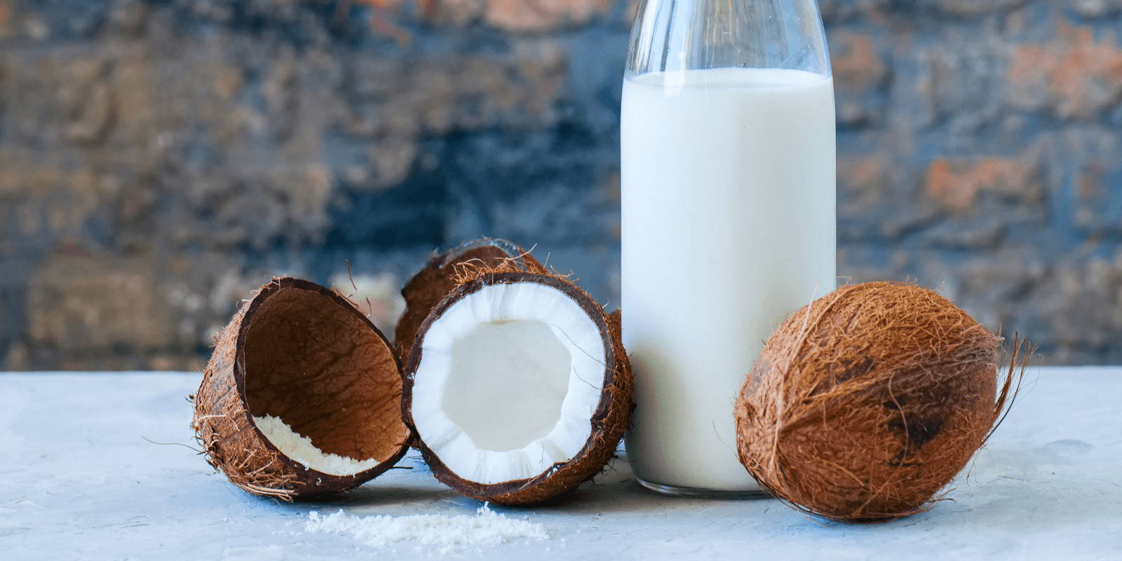 A jug of coconut milk on a white table, styled with coconuts.