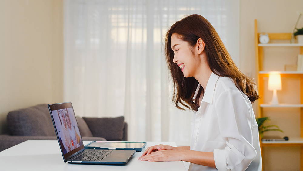 Asian woman talking and laughing in a videoconference at her laptop