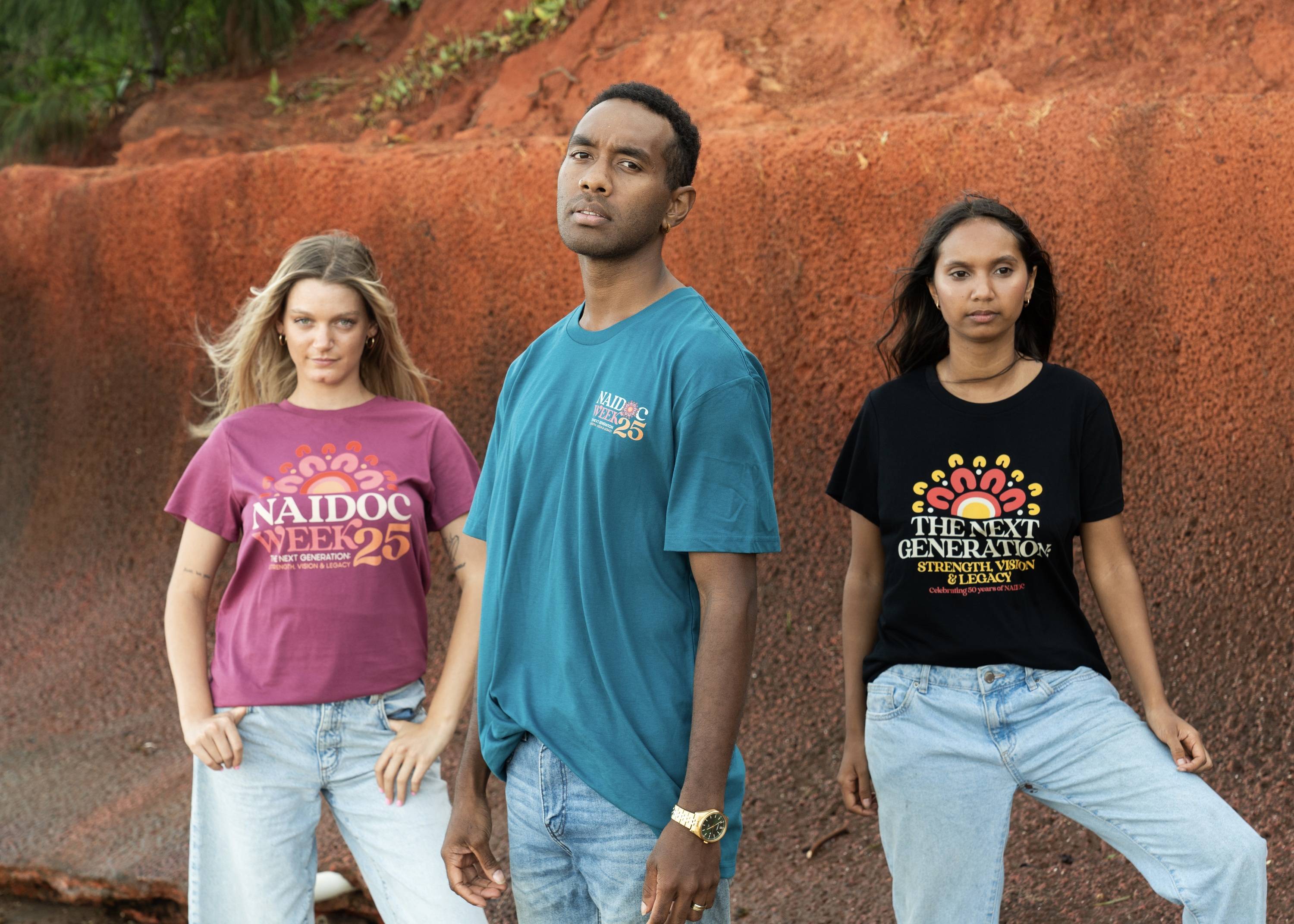 three Indigenous models wearing Yarn's NAIDOC logo on t-shirts standing in front of red earth