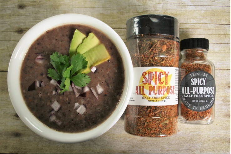A bowl of spicy black bean soup next to a large and small bottle of FreshJax Organic Spicy All-Purpose Spice.
