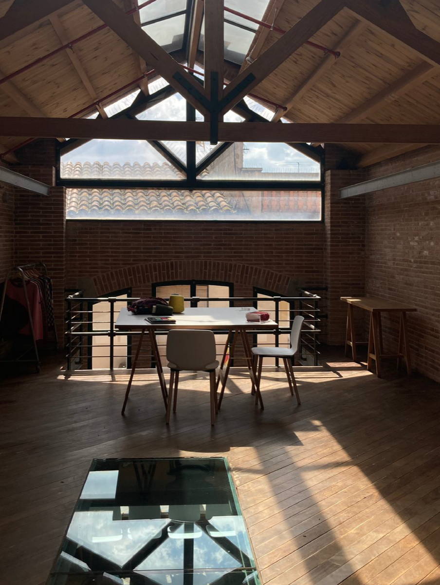 Interior d' un espai amb terra de fusta i llum natural amb finestrals i una taula gran al centre. 