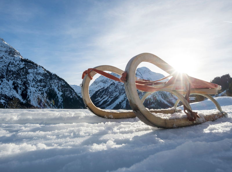 Rodeln vor verschneiter Bergkulisse im Kleinwalsertal.