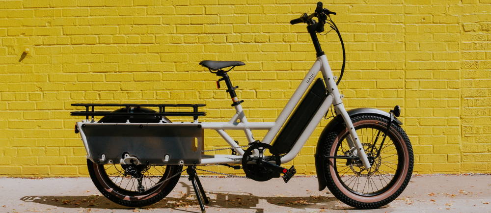 a white Specialized Globe Haul electric cargo bike against a yellow brick wall