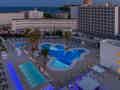 Moderner Hotelpoolbereich mit blauer Beleuchtung, Palmen und Meerblick in der Abenddämmerung.