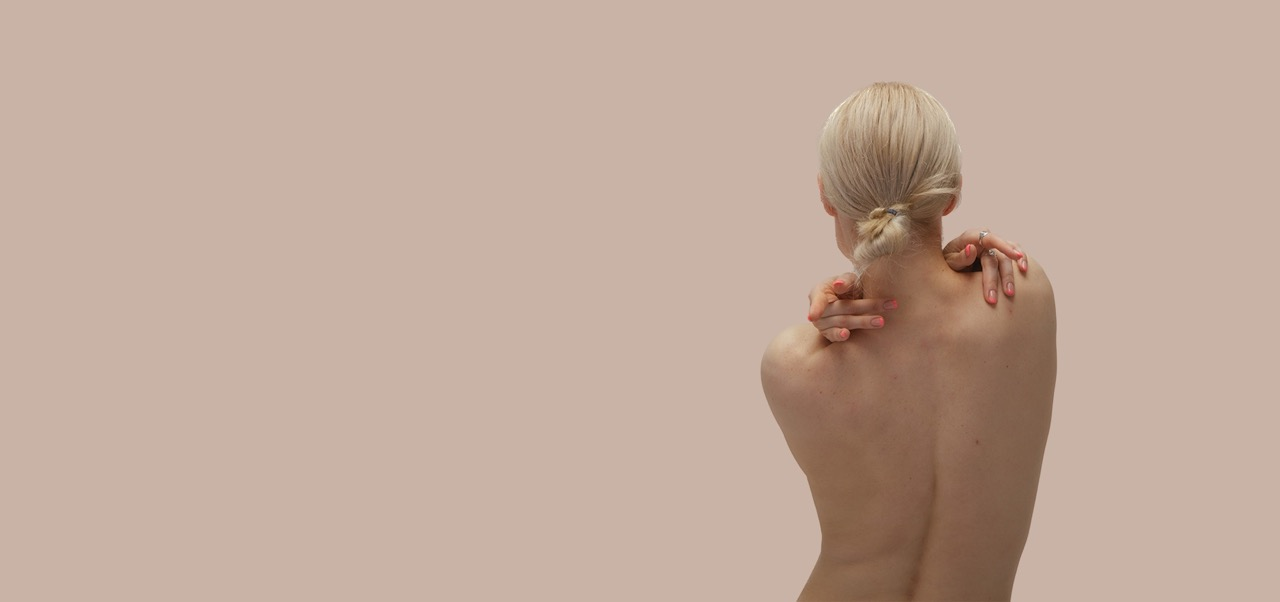 nackter Rücken einer blonden Frau vor beigem Hintergrund