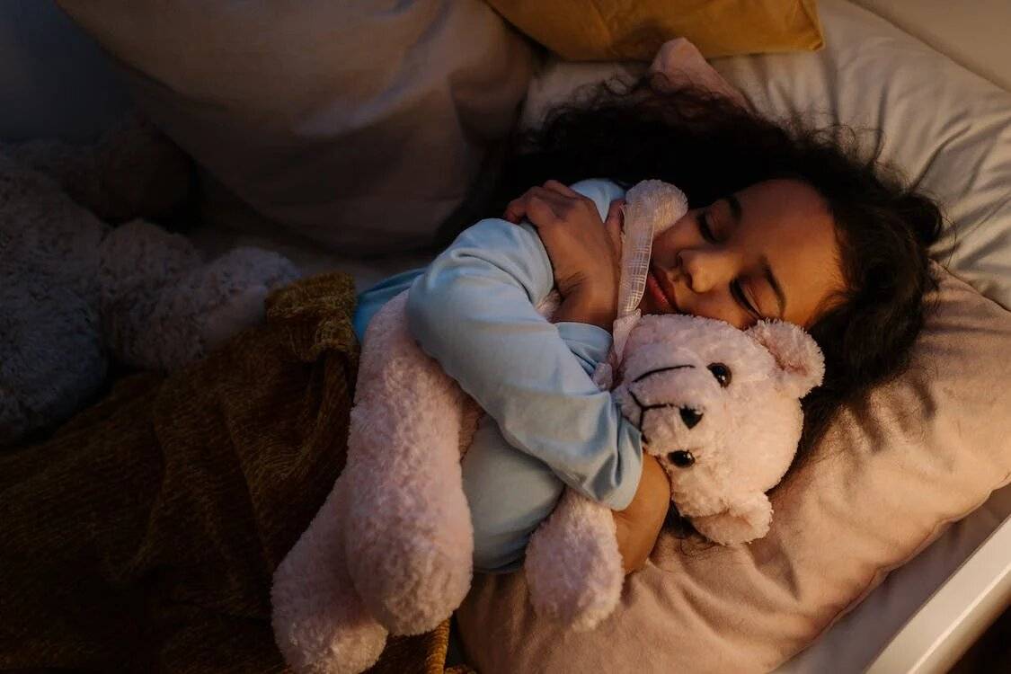 A little girl snuggled up with her teddy bear in bed, resting peacefully - Photo by cottonbro from Pexels