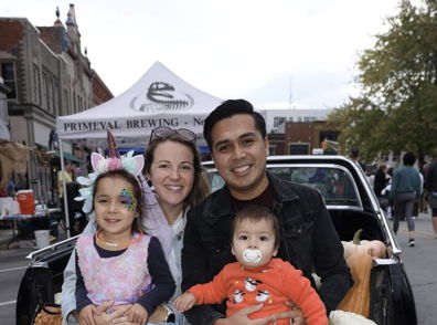 A joyful family of four sits together at a festive outdoor event surrounded by pumpkins, radiating happiness and connection.