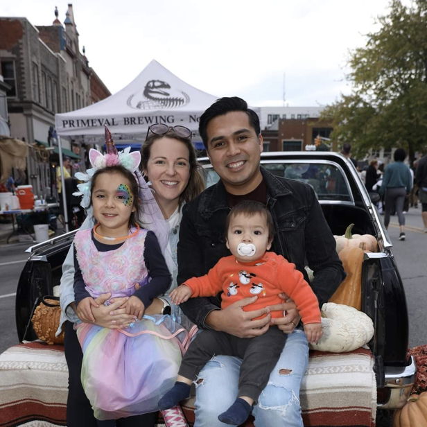 A joyful family of four sits together at a festive outdoor event surrounded by pumpkins, radiating happiness and connection.
