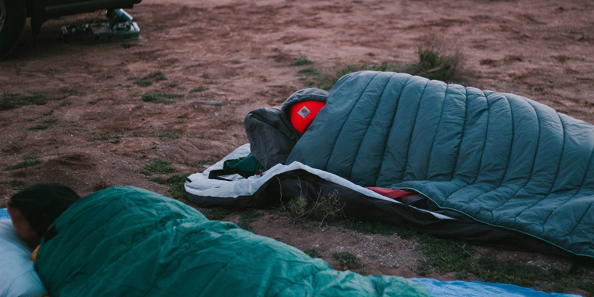 Man sleeping on the ground under a Rumpl camping blanket