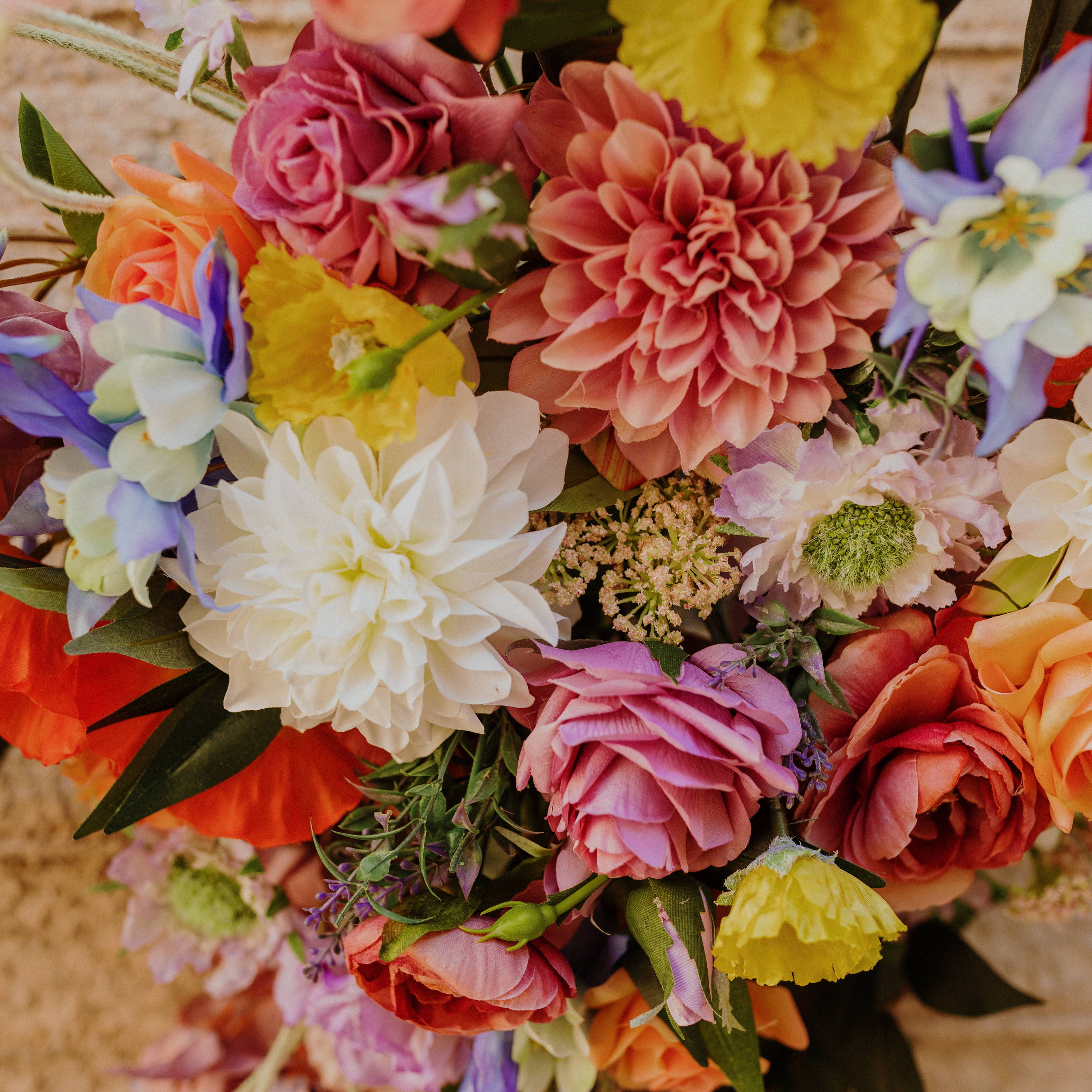 A very colorful and whimsical wedding flora backdrop including Columbines, white and mauve dahlias, mauve roses, and yellow poppies. 