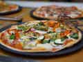 Gemüsepizza mit Paprika, Zwiebeln und Zucchini auf einem schwarzen Teller mit Pizzaschneider.