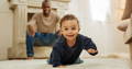 Little boy crawling on the bedroom floor while his father looks at him from behind and smiling.