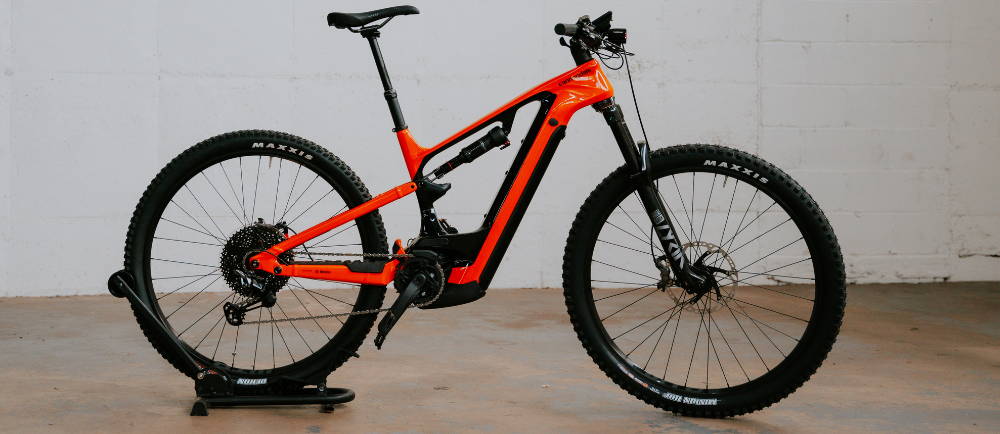 a red Cannondale Moterra electric full suspension mountain bike against a white wall