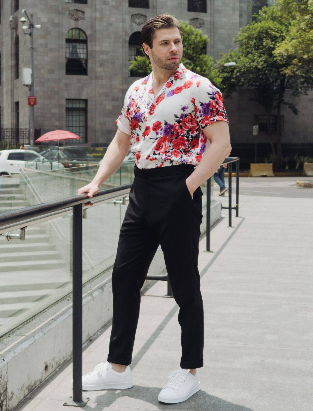 model standing in a plaza wearing white shoes black high rise pants and a short sleeve white floral silk shirt from 1000 kingdoms