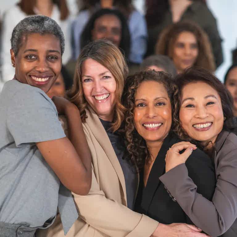 Diverse group of smiling women hugging closely, posing for a photo at a gathering.