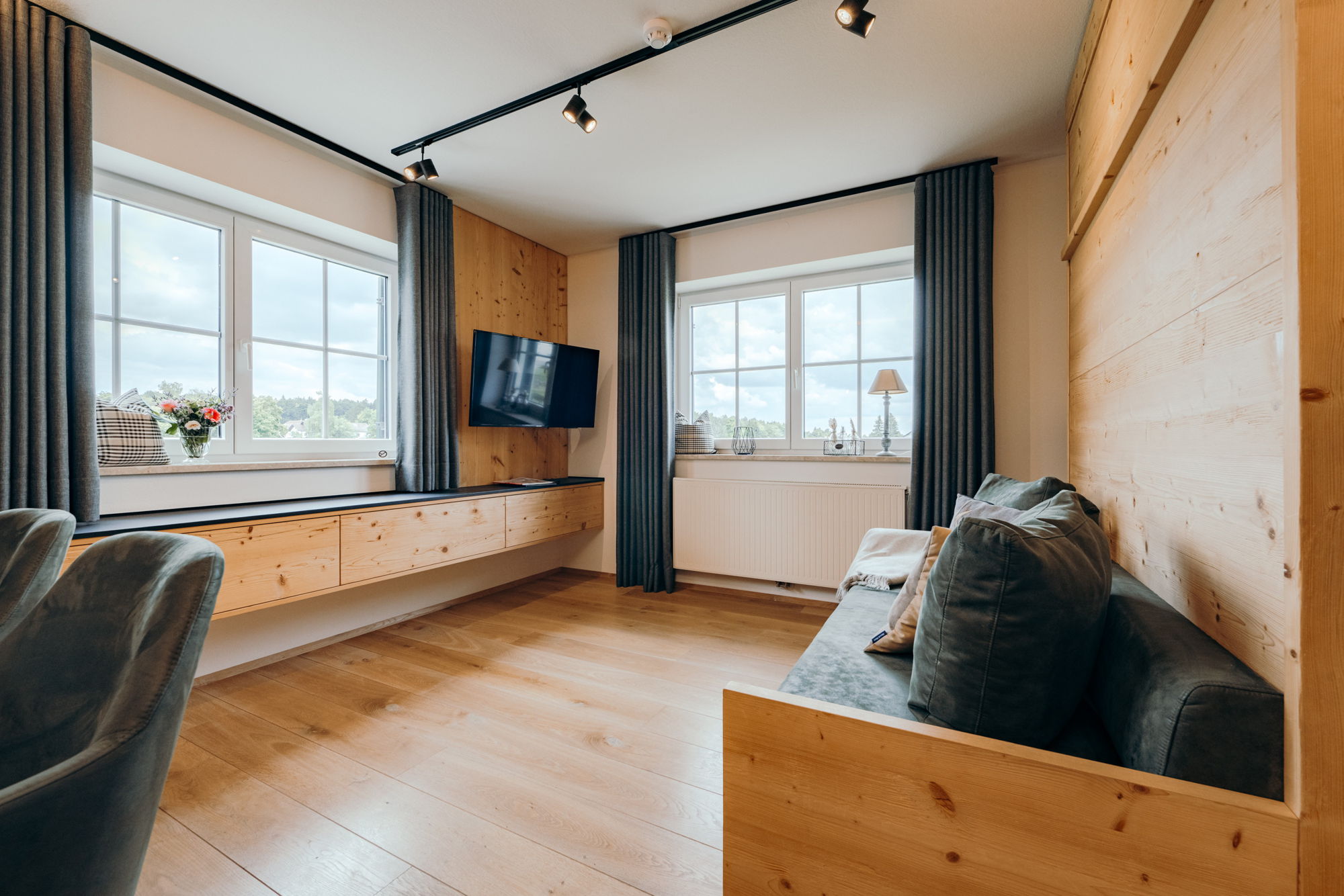 Ein Wohnzimmer mit hellem Holz, grauen Gardinen und einem gemütlichen Sofa.