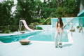 a woman wearing pink skates and a matching pink crop top with geometric pants stands in front of the pool for poolside pride: a slim aarons-inspired pride campaign