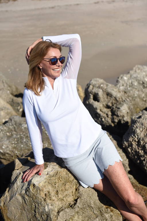 Val wears a white sun shirt on the beach.