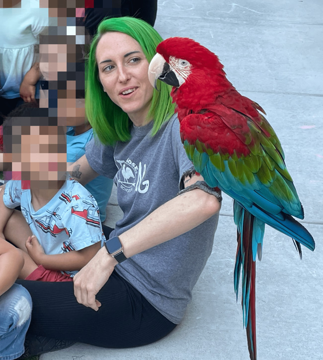 ms. brianna, a primrose preschool teacher, sitting with a colorful parrot on her arm
