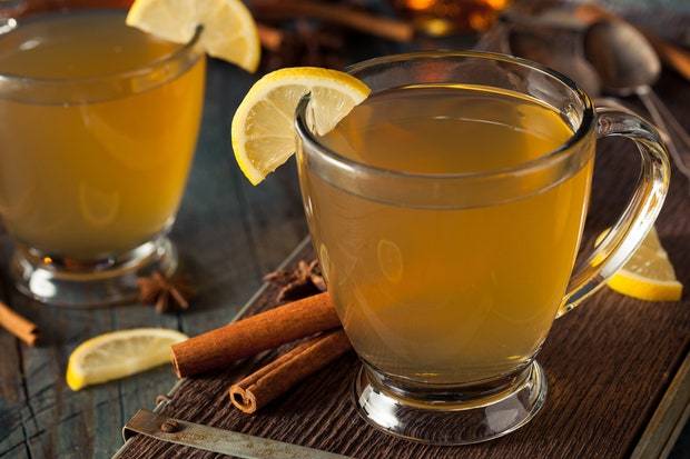 clear mug with yellow drink with lemon slice and cinnamon stick