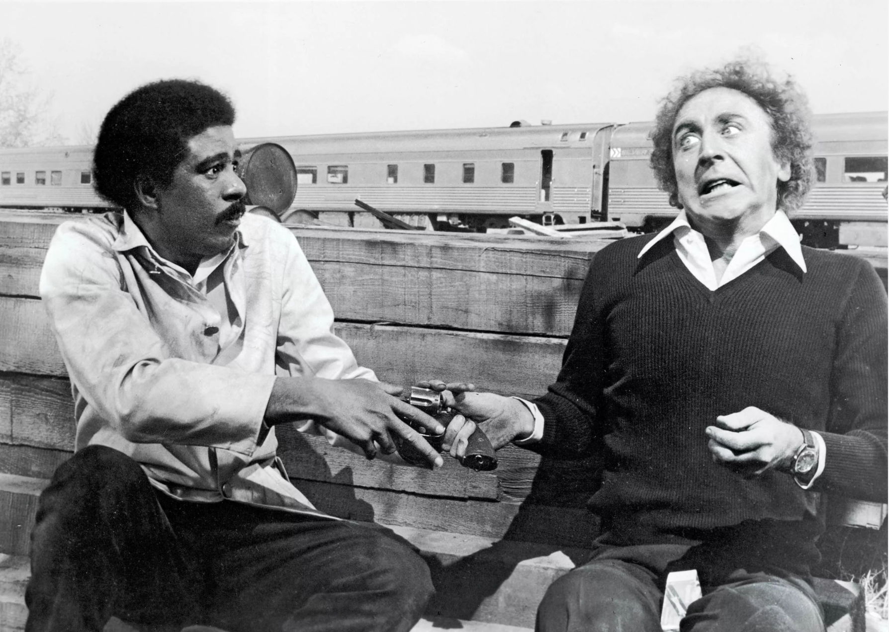 Richard Pryor on the set of a movie with fellow actor holding  a prop gun during a scene.