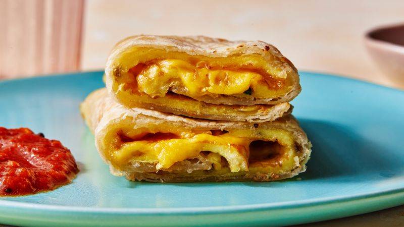 Straight-on shot of a roti omelet roll-up with sambal oelek on the side, and american cheeze oozing out