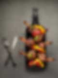 Skewers of chicken lollipops and colorful bell peppers on a metal tray with a red napkin, knife, and fork