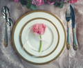 dinner and charger plates with a rose on top and silverware on the sides over a pink tablecloth