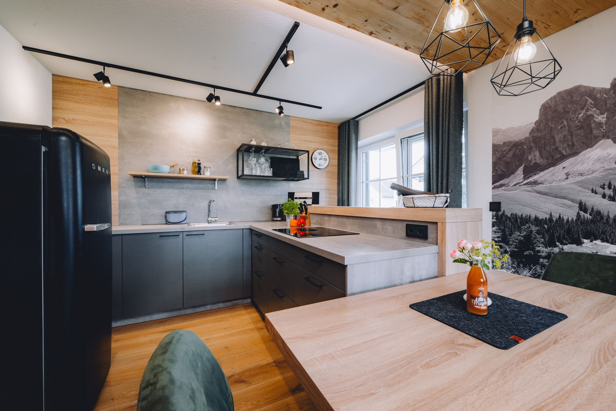 Eine moderne Küche mit Holzwand, steinernen Arbeitsflächen und einem schwarzen Kühlschrank.