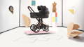 Cybex Platinum campaign image showcasing three luxury baby strollers (Mios, Priam, and Coya) in a modern minimalist room, with black and rose gold finishes, styled on colorful platforms alongside decorative wall art and the text “The New Luxury of Travel.”