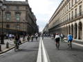 Des cyclistes et des piétons se déplacent sur un grand boulevard parisien flanqué par des bâtiments historiques