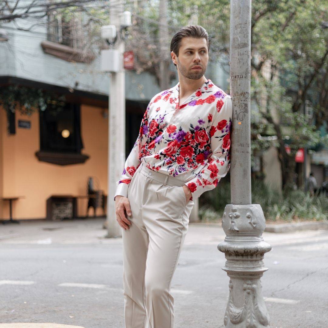 model leaning against a street post wearing khaki colored pants and a long sleeve white floral silk shirt from 1000 kingdoms