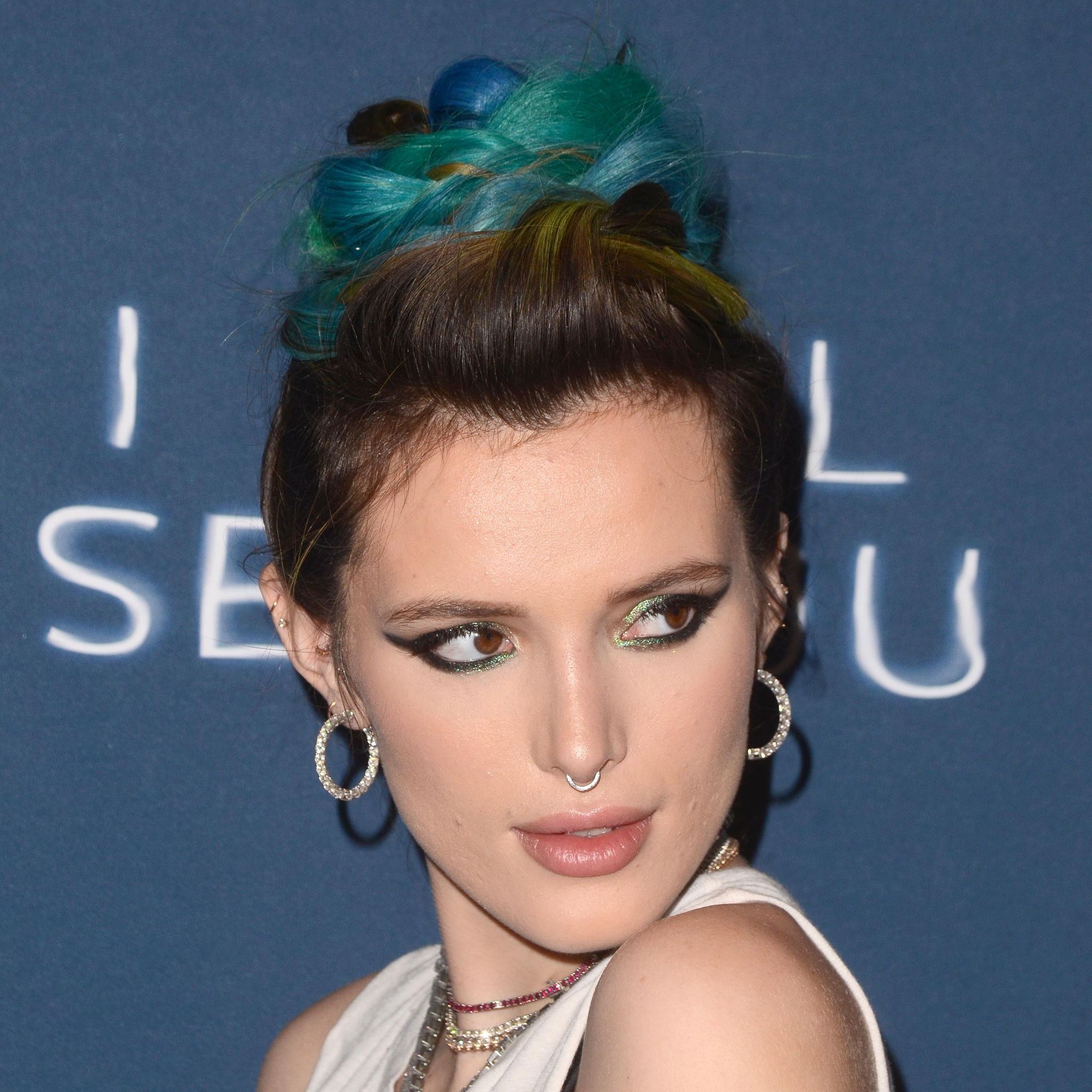Bella Thorne posing while at a press event wearing a dress and blue hair.