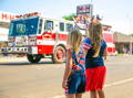Two girls standing on the sidewalk and looking at the passing firetruck. 
