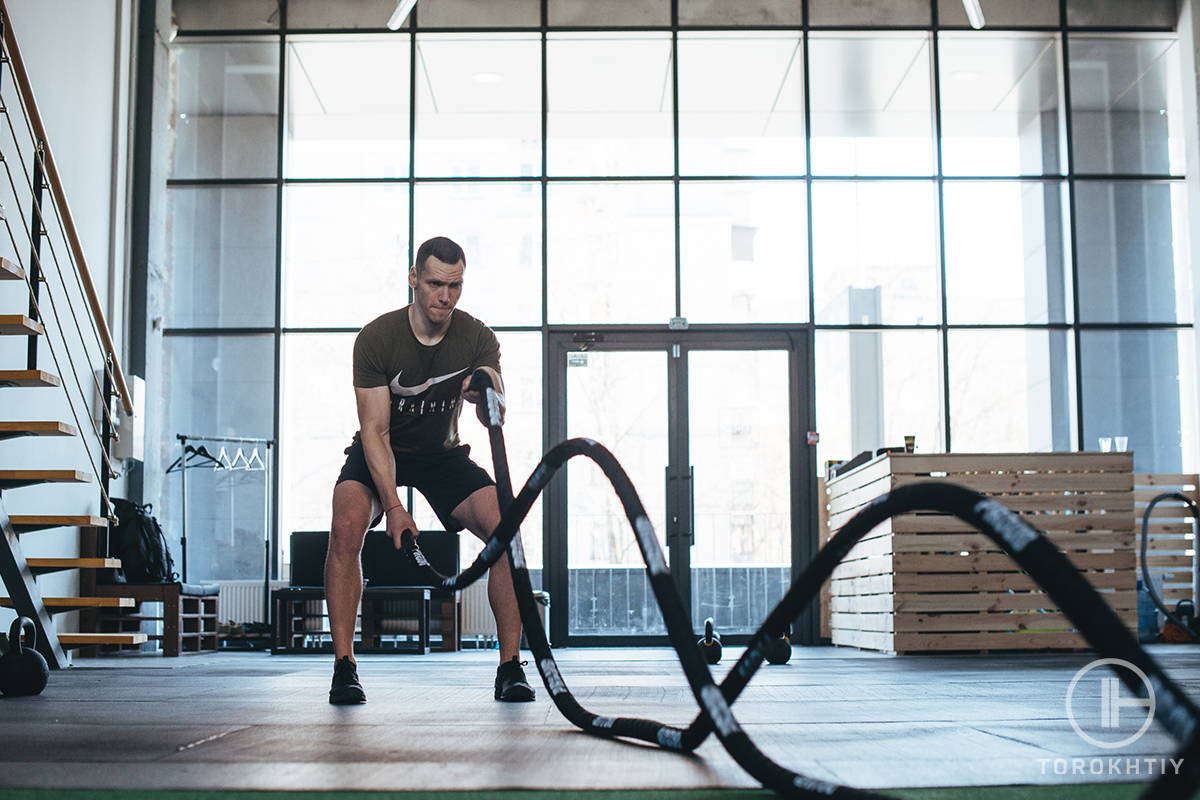 athlete training his muscles with battle rope at gym