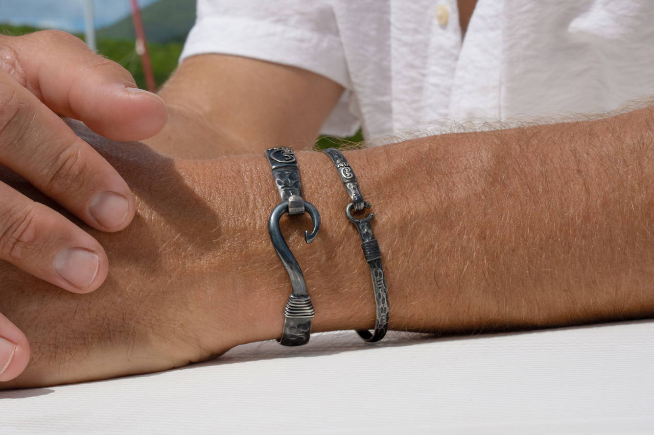 A man's hand wearing ocean fishhook bracelets.