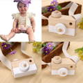 Wooden Camera toy with a white finish, shutter button, and adjustable strap, and a little girl wearing it around her neck.