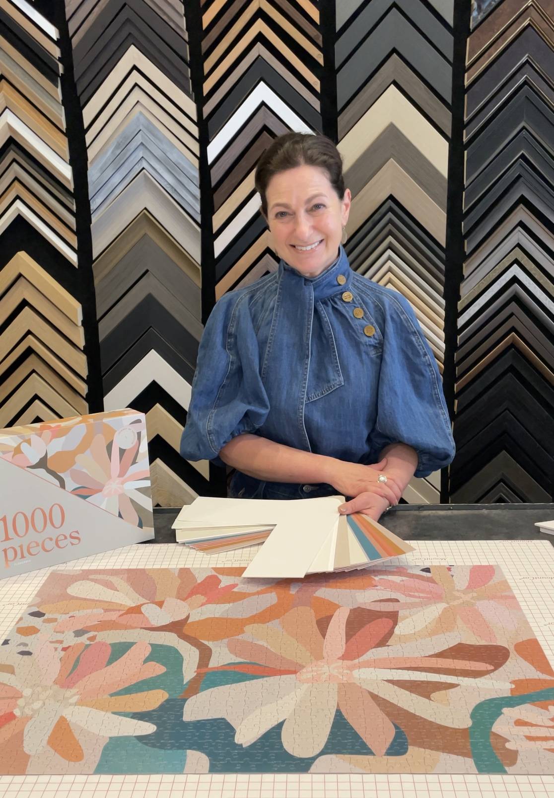 Cath holding a selection of mat board colours next to an art puzzle 