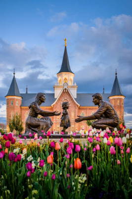 Provo City Center Temple picture. A statue of a mother and father teaching their child to walk stands in front of the temple surrounded by tulips.