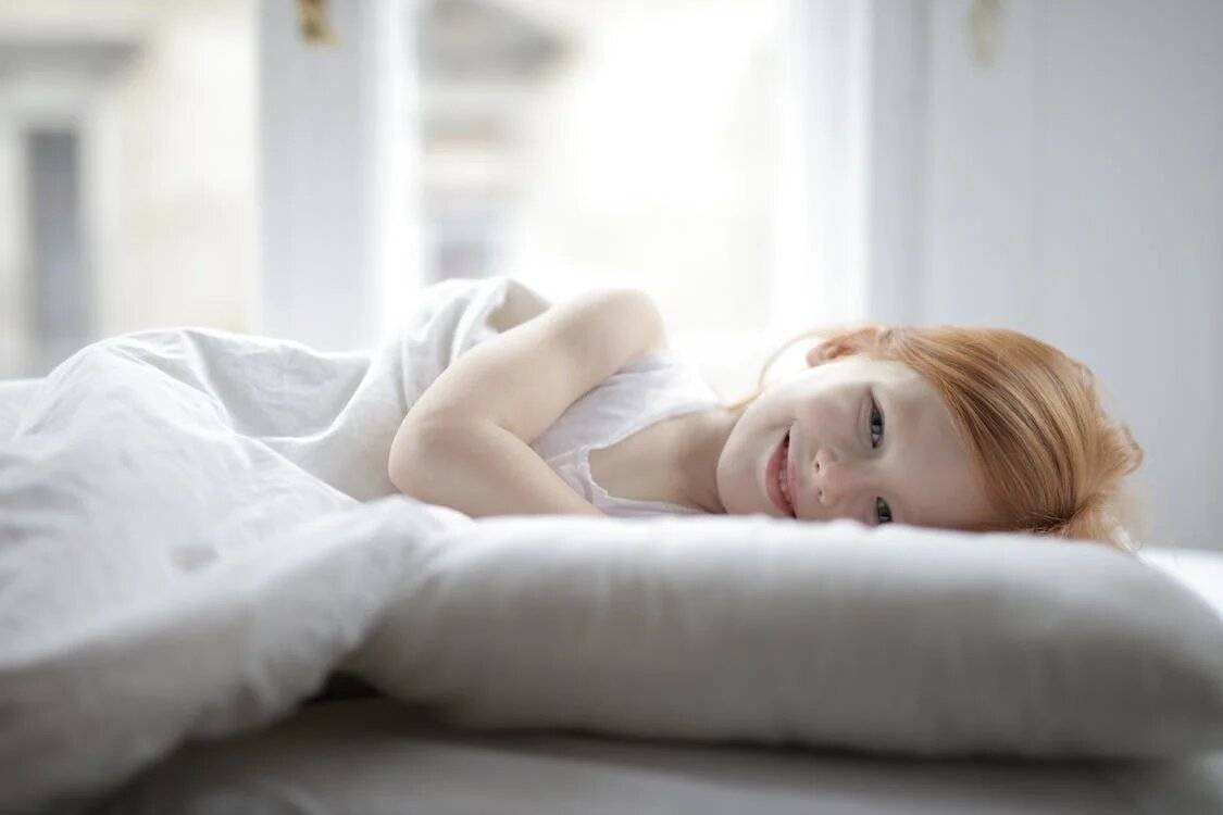 Girl in white tank top lying on white bed sheets