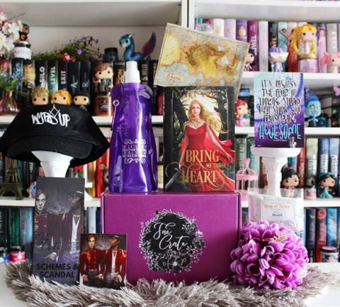 June 2018 Schemes & Scandals box theme included Bring Me Their Hears by @authorsarawolf, "Wyrd Up" Hat, Cruel Prince Bend-A-Bottle, King of Scars Bath Tea, Selection Crown Hair Clip, Selection Art Print, Darker Shade of Magic Magnet, Darker Shade of Magic T-Shirt, and E-Book Download of The Affiliate and Map by @authoralinde. 