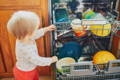 Toddler standing next to a dishwasher.