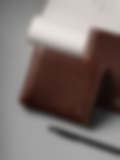 Two premium brown leather wallets placed on a gray surface, accompanied by a pen, showcasing a sophisticated handcrafted design.